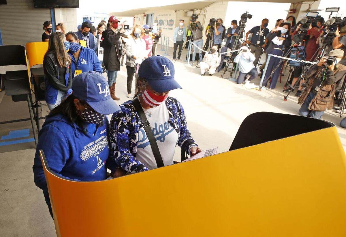 Two people in masks and Dodgers hats and shirts stand at a voting booth.