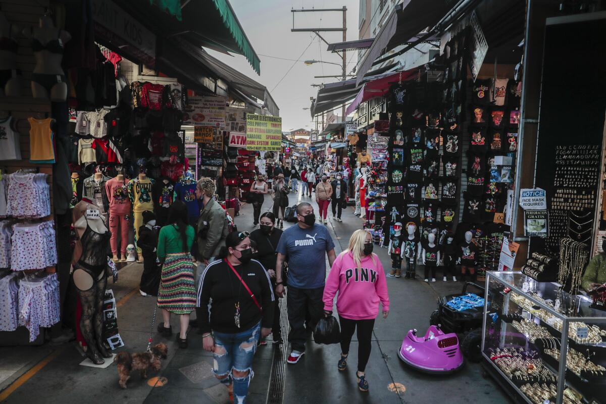 People in masks walk on a pedestrian roadway surrounded by shops' goods.