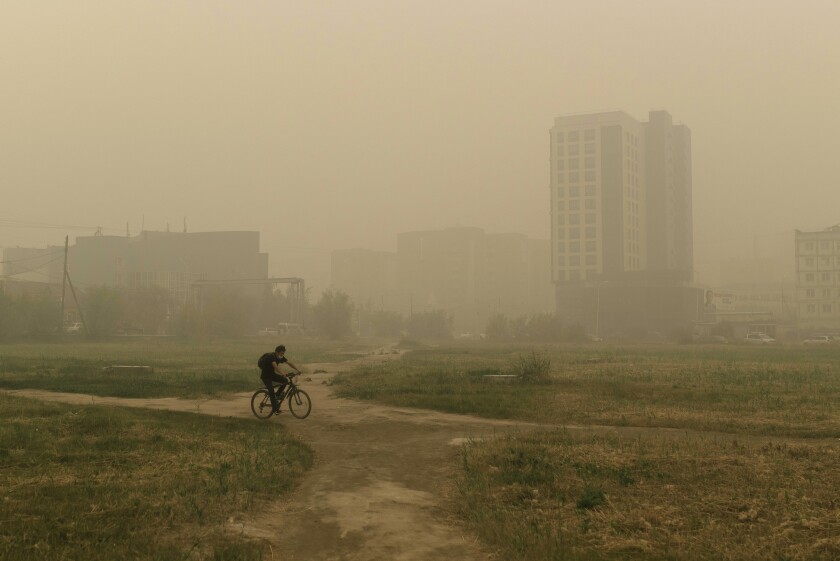 FILE A man rides his bicycle through smoke from a forest fire covers Yakutsk, the capital of the republic of Sakha also known as Yakutia, Russia Far East, Russia, Thursday, Aug. 12, 2021. The U.N. weather agency has certified a 38-degree Celsius (100.4 Fahrenheit) reading in the Russian town of Verkhoyansk last year as the highest temperature ever recorded in the Arctic. The World Meteorological Organization said the temperature "more befitting the Mediterranean than the Arctic" was recorded in June 2020 during a heat wave that swept across Siberia and stretched north of the Arctic Circle. Average temperatures were up to 10 degrees Celsius more than usual in Arctic Siberia. (AP Photo/Ivan Nikiforov, File)
