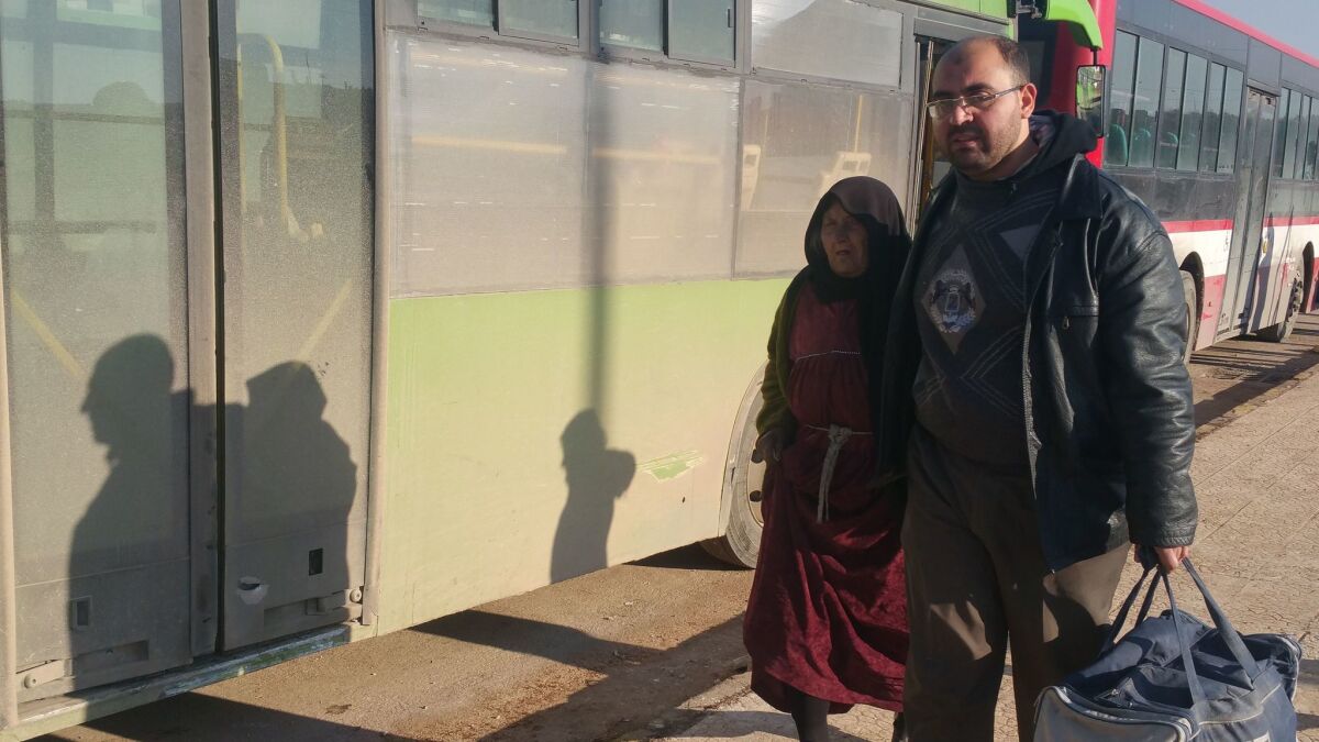 Mustafa Sello and his mother, Fatemah, leave Ramousseh crossing after her evacuation from east Aleppo.