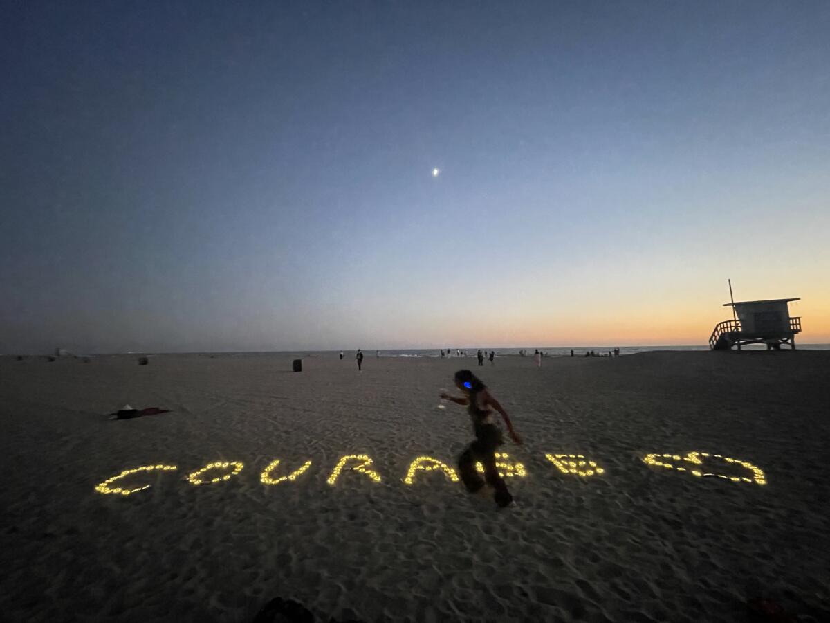 The word COURAGE is illuminated with lights on the beach beside the shape of a heart. 