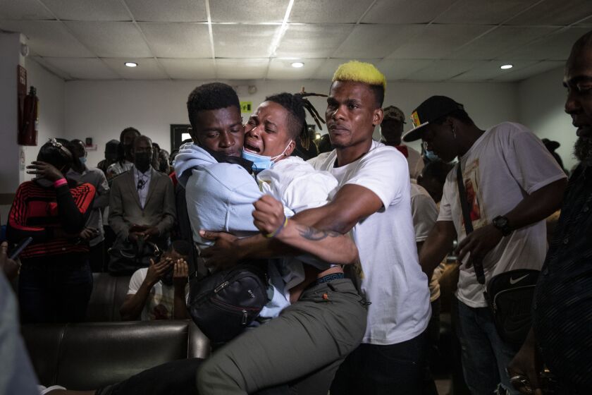 Eldyne Archange, center, mourns the loss of her brother as her cousin, Guinot Valdez, right, and another man hold her as friends, families and supporters gather in a small funeral home to remember the lives of Jocelyn Anselme, 34, and Calory Archange, 30, two Haitians who died living in Mexico on Thursday, June 2, 2022 in Tijuana, Mexico. Anselme was killed and Archange died of a heart attack. Anselme and Archange have been stuck in Tijuana because of Title 42, a program that prevents asylum seekers and other undocumented immigrants from crossing in to the United States.