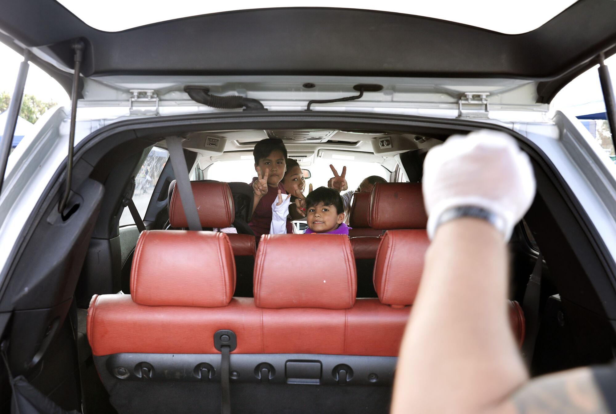Parents, two kids look out the back of their minivan and flash the peace sign at a volunteer holding a fist in the air.
