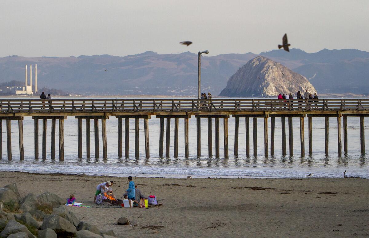 Una toma del histórico muelle de Cayucos con Morro Rock en la distancia y las imponentes chimeneas de la central eléctrica de Morro Bay.