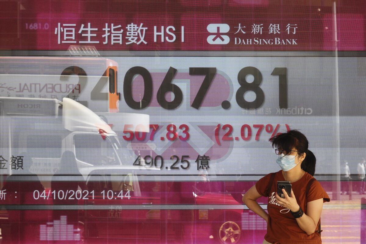 A woman walks past a bank's electronic board showing the Hong Kong share index at Hong Kong Stock Exchange in Hong Kong Monday, Oct. 4, 2021. Asian markets were mixed on Monday, while Hong Kong’s benchmark shed more than 2% after troubled property developer China Evergrande’s shares were suspended from trading. (AP Photo/Vincent Yu)