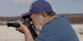 A side view of a man holding up and pointing a big camera.