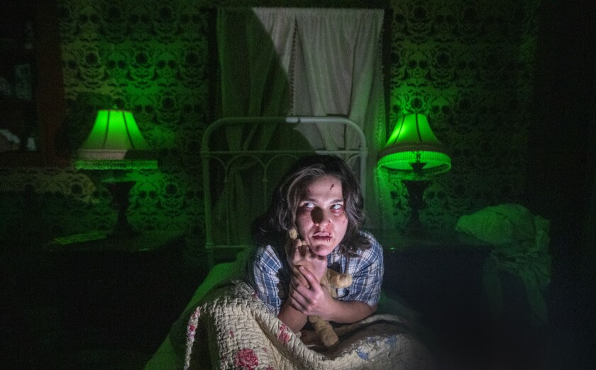 A woman huddled in a dark room is backed by glowing green lamps.