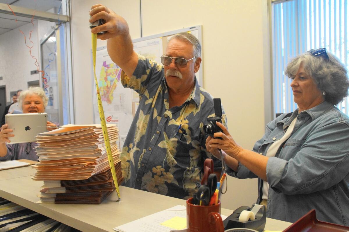 Jay Humphrey of Costa Mesa First measures the height of petition paperwork that he and others presented to the Costa Mesa city clerk's office on Jan. 4 as Mary Spadoni, left, and Sally Humphrey take photos.