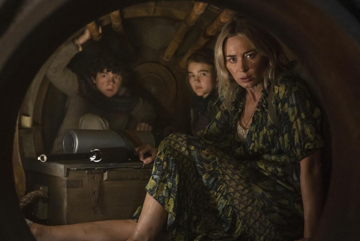 Two children and a woman sit in a cramped dark space in a scene from "A Quiet Place Part II."