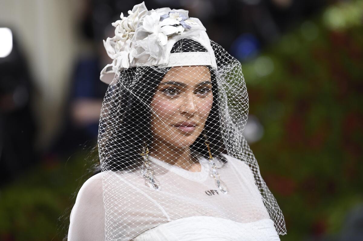 A woman in white wears a hat with a veil
