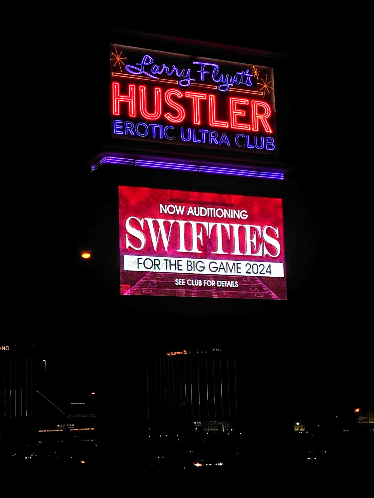 A lighted Hustler Club sign at night announces auditions for Taylor Swift fans.
