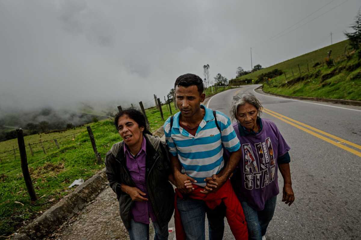 Luis Mario Fuenmayor Alfaro ayuda a Liliana Mendoza, izquierda, y a su madre, Eva Alfaro Aldana a subir una última colina antes de llegar a una estación de la Cruz Roja en La Laguna, Colombia.