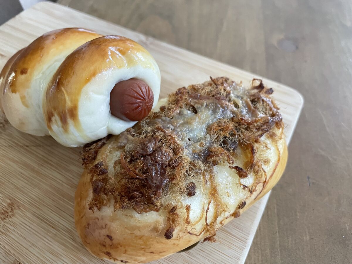 Two puffed baked goods, one with the end of a hot dog protruding from it, on a wooden cutting board.