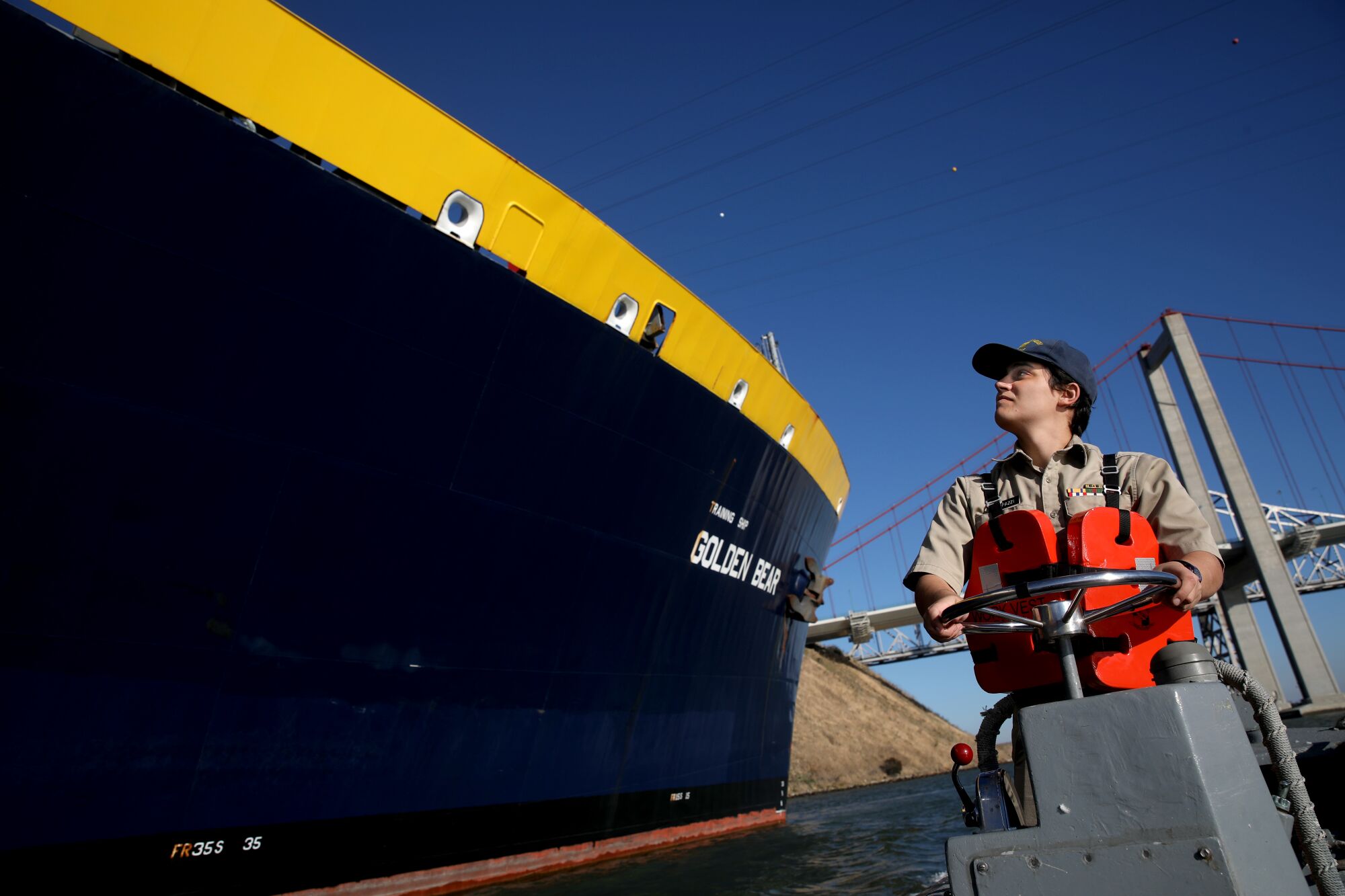 A person turns a circular metal object next to a ship.