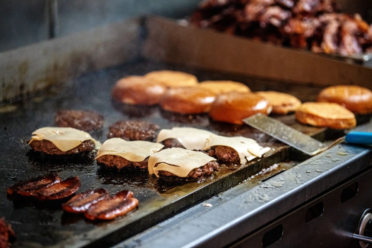 Hamburgers and buns sit atop a hot grill. 