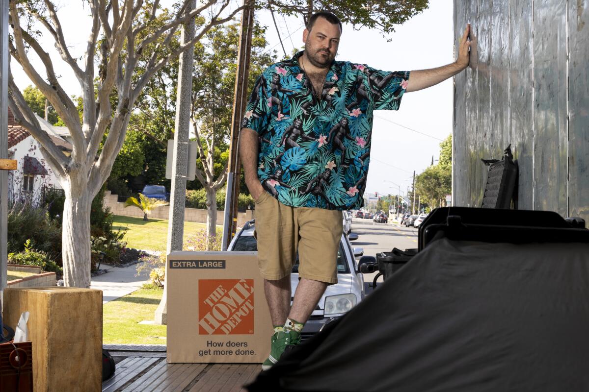 A man standing outside a home with a number of moving boxes at his feet