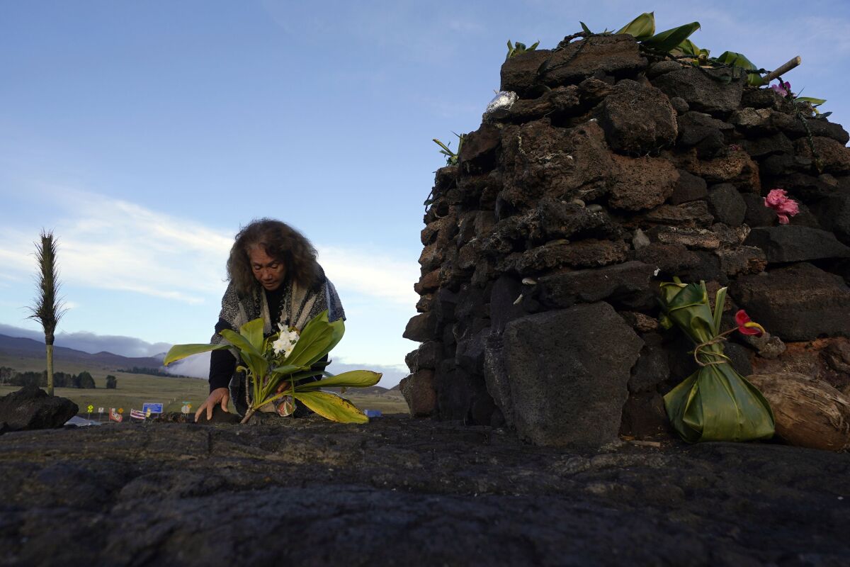 Illona Ilae, of Kailua-Kona, Hawaii, leaves an offering in front an alter below the Mauna Loa volcano as it erupts Thursday, Dec. 1, 2022, near Hilo, Hawaii. Glowing lava from the world's largest volcano is a sight to behold, but for many Native Hawaiians, Mauna Loa's eruption is a time to pray, make offerings and honor both the natural and spiritual worlds. (AP Photo/Gregory Bull)