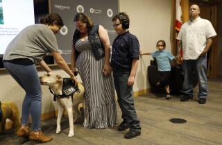 Service dog Justice gets his service vest while new handler, Lauren Shrader, and her son, Aiden, who is on the autism spectrum, look on during a graduation ceremony on Saturday in La Jolla for Good Dog! Autism Companions, a Fallbrook nonprofit that trains and places service dogs with families with children who have autism as well as with autism therapists.