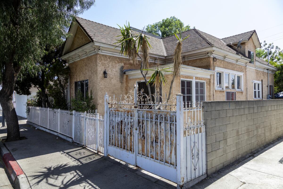 A beige stucco house surrounded by a white metal and brick fence.