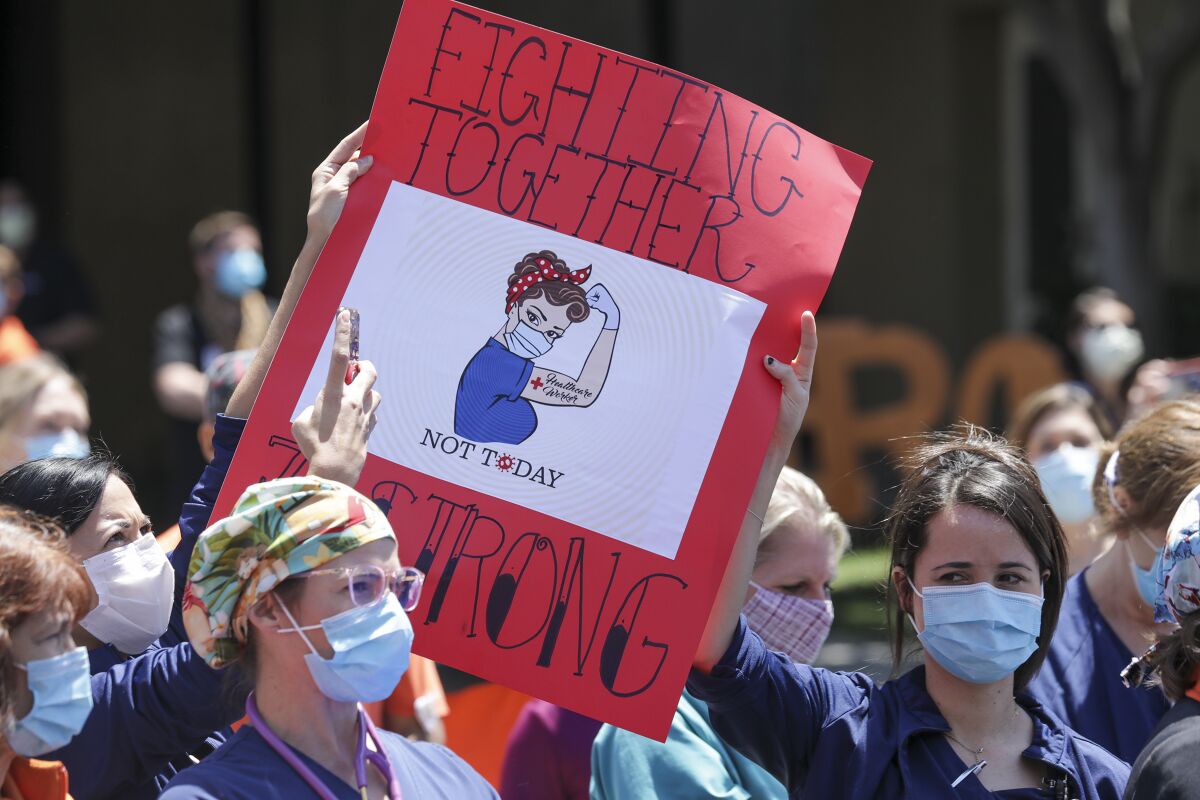 Healthcare workers wearing masks hold a sign that says "fighting together" with a drawing of a nurse flexing her muscle