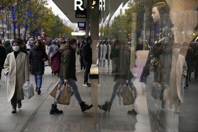 A woman is reflected as she walks into a shop on Oxford Street in London, Monday, Nov. 29, 2021. Countries around the world slammed their doors shut again to try to keep the new omicron variant at bay Monday, even as more cases of the mutant coronavirus emerged and scientists raced to figure out just how dangerous it might be. In Britain, mask-wearing in shops and on public transport will be required, starting Tuesday. (AP Photo/Matt Dunham)