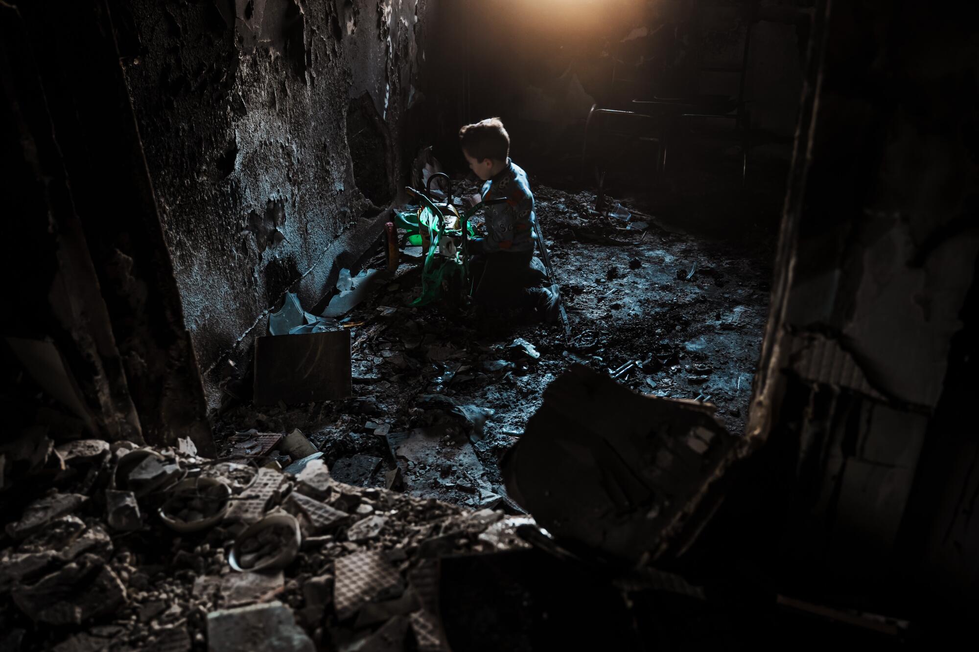 Hamzeh Sabbagh, 5, tries to recover and play with his charred tricycle inside the ruins of his home.