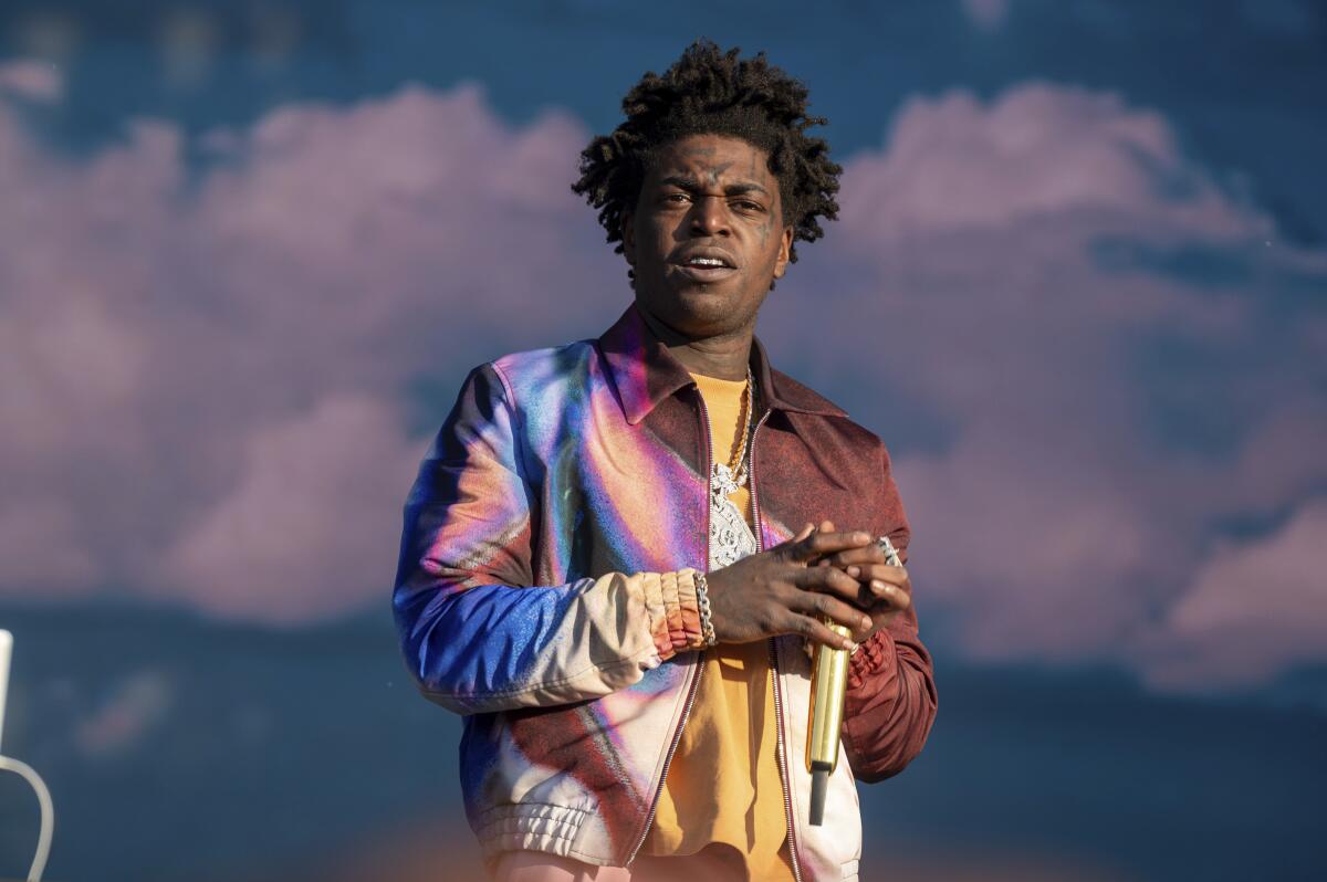 Kodak Black holds a golden microphone while wearing a colorful bomber jacket