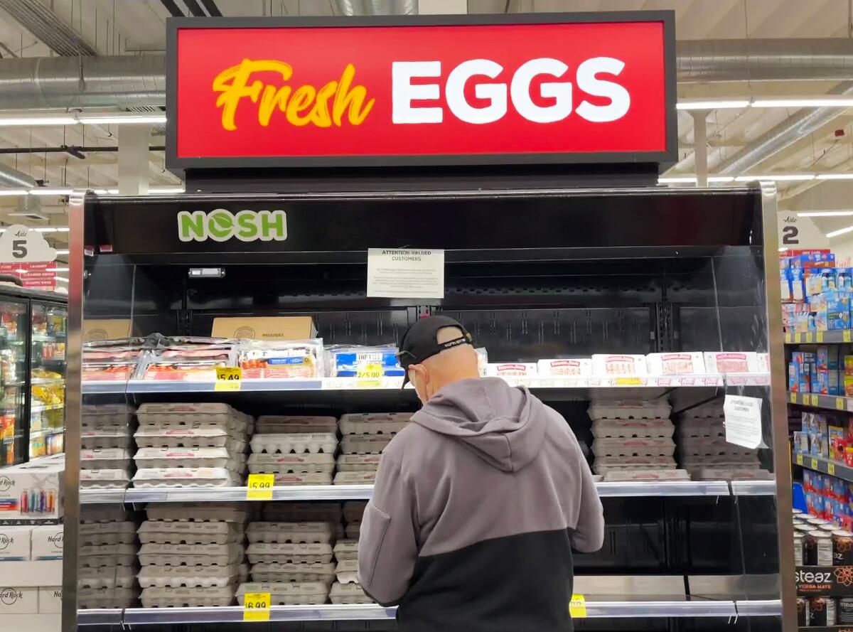 A man stands in front of a depleted refrigerated egg display case at a grocery store