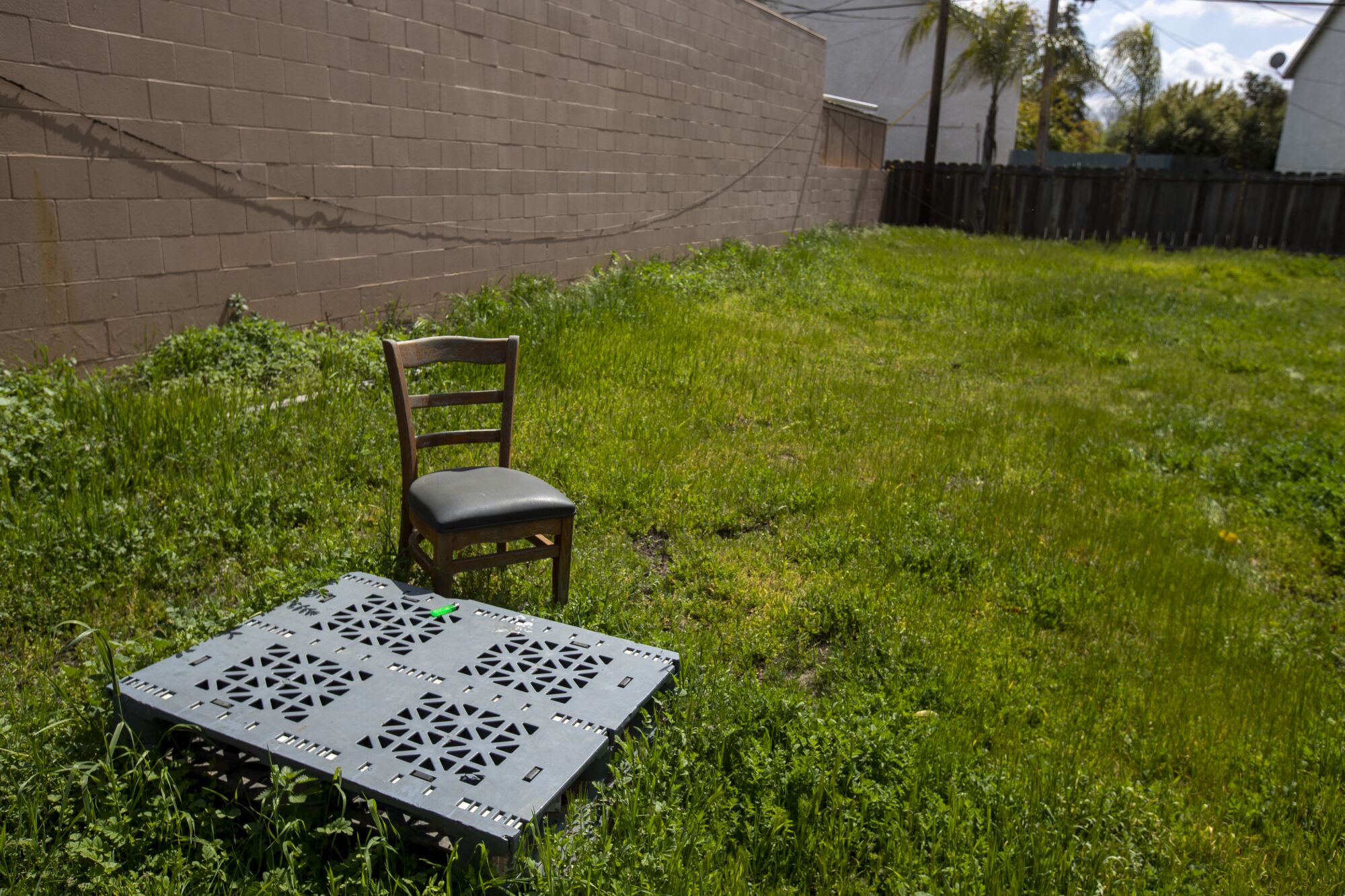 A grassy lot with a square, metal covering and a chair.