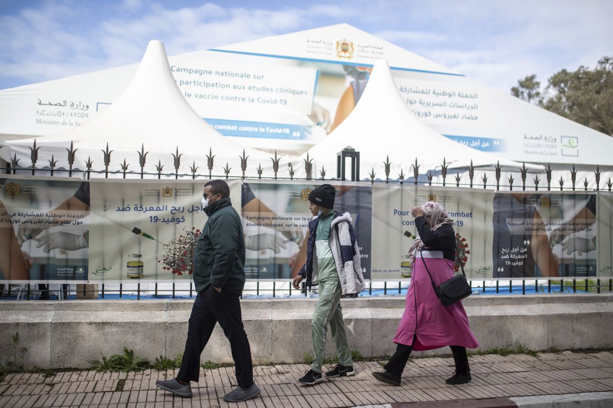 People wearing face masks to prevent the spread of coronavirus walks past a bivouac where clinical trials for covid-19 vaccines are conducted, in Rabat, Morocco, Monday, Dec. 7, 2020. (AP Photo/Mosa'ab Elshamy)
