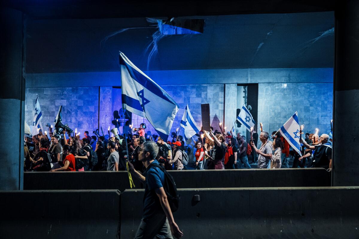 People carrying blue-and-white flags walk past illuminated buildings at night
