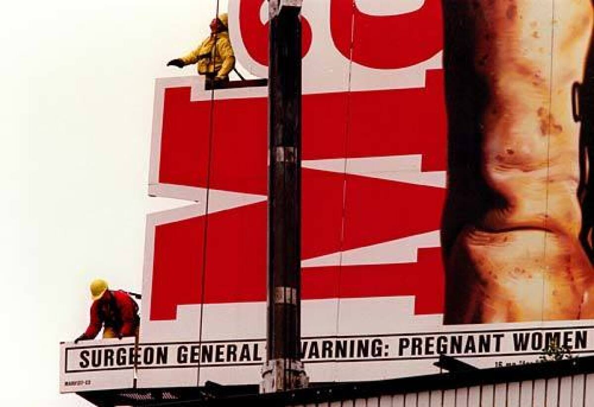 A color photograph shows workers in harnesses removing a portion of a Marlboro billboard