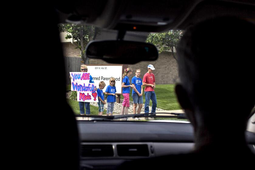 Dr. Carol Ball, at right in car, arrives at the Planned Parenthood clinic in Sioux Falls, S.D., as protesters Sara Beaner and five of her seven children stand outside the clinic with a sign that reads, "You are wonderfully made."