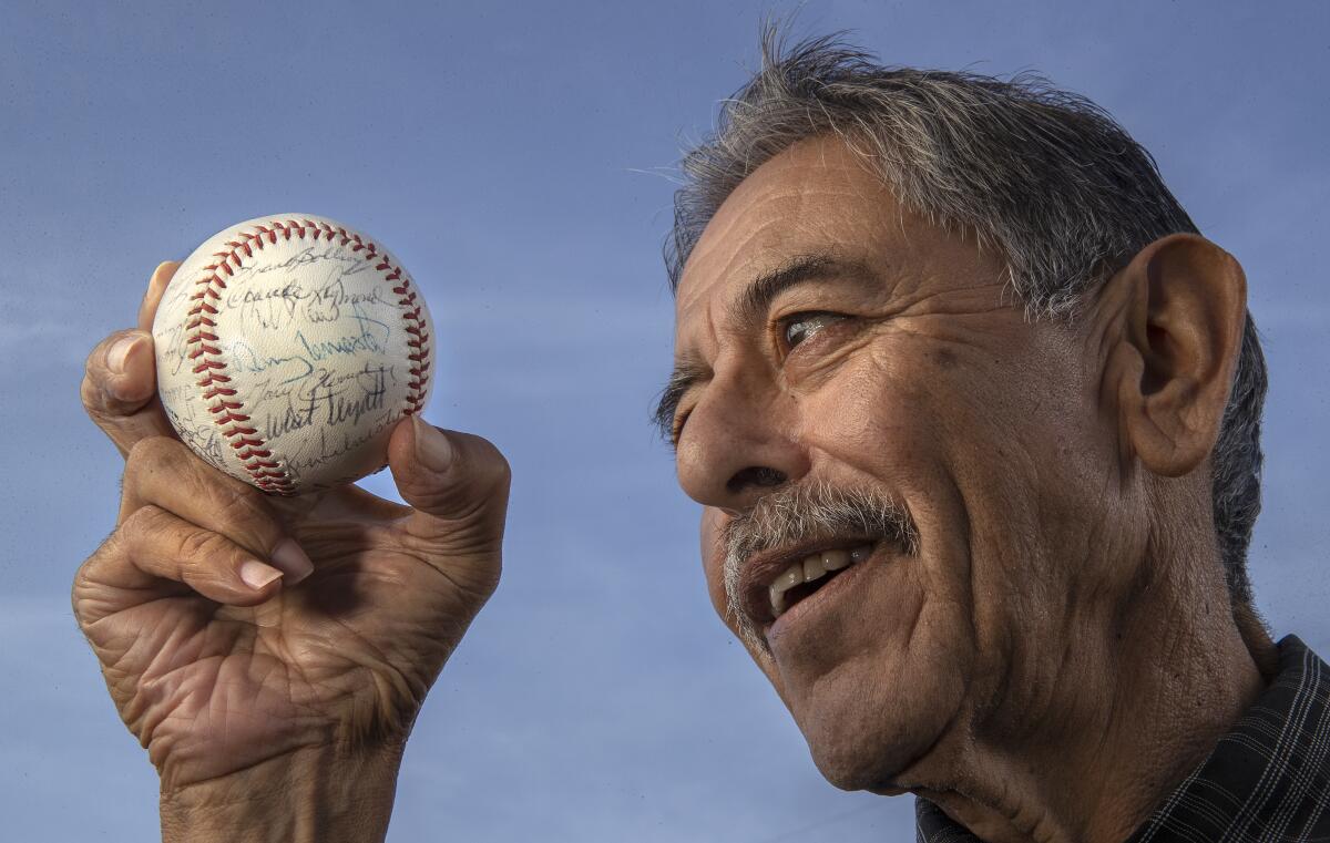 a man with a mustache looks at a signed baseball that he holds in his hand