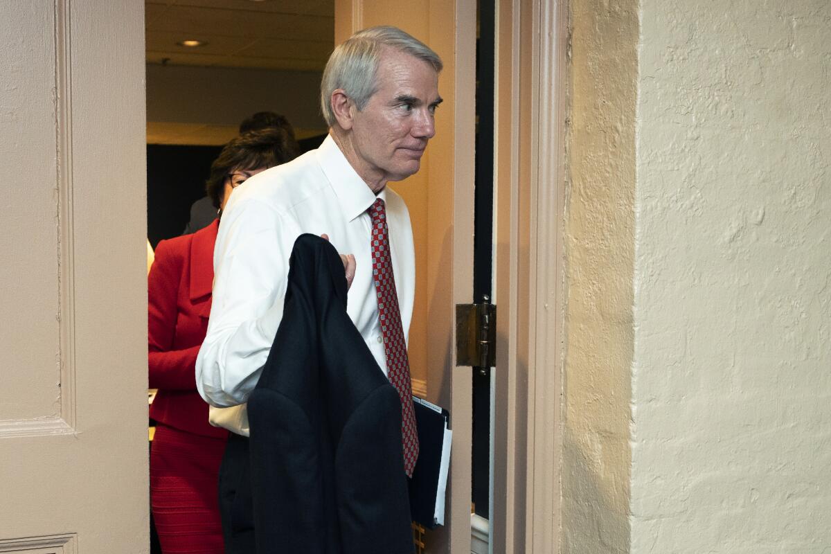 Sen. Rob Portman, holding his jacket, walks out of a door. 