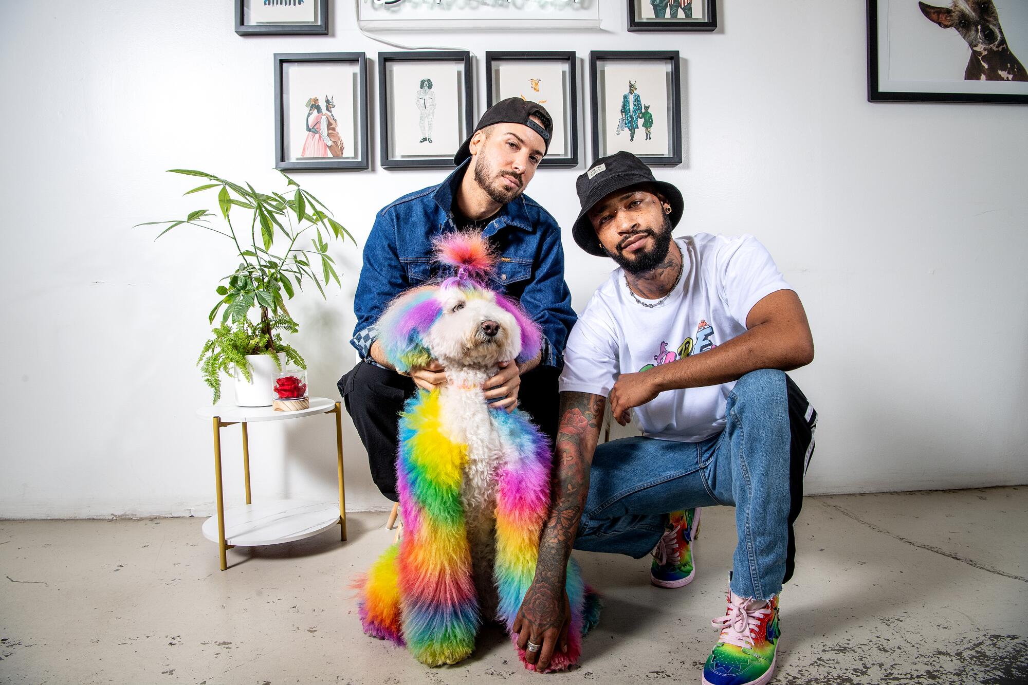 A man sits and another kneels with a tie-dyed dog 