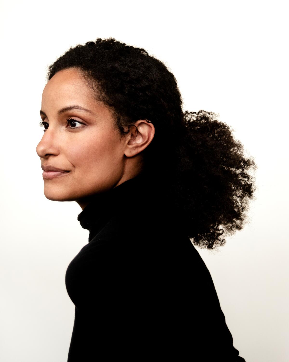 Author Kiley Reid, in a black turtleneck, smiles with her head turned to the side.