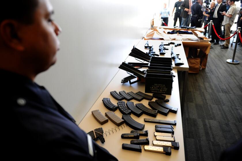 An officer stands by a cache of weapons that were found at the home of Daniel Yealu, the man accused of shooting one officer in the lobby of a police station.