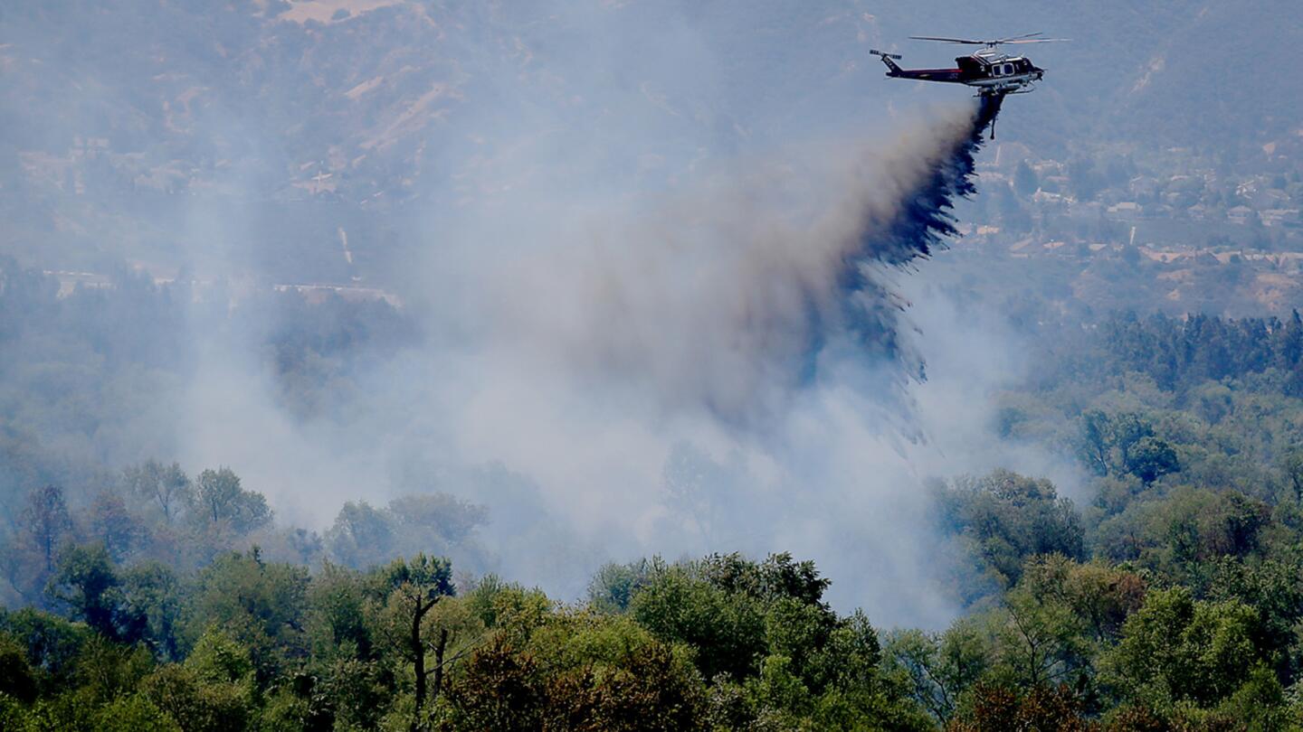 A helicopter drops fire retardant in the bed of the Santa Ana River in an attempt to contain a brush fire that continued to burn near Prado Dam on Sunday.