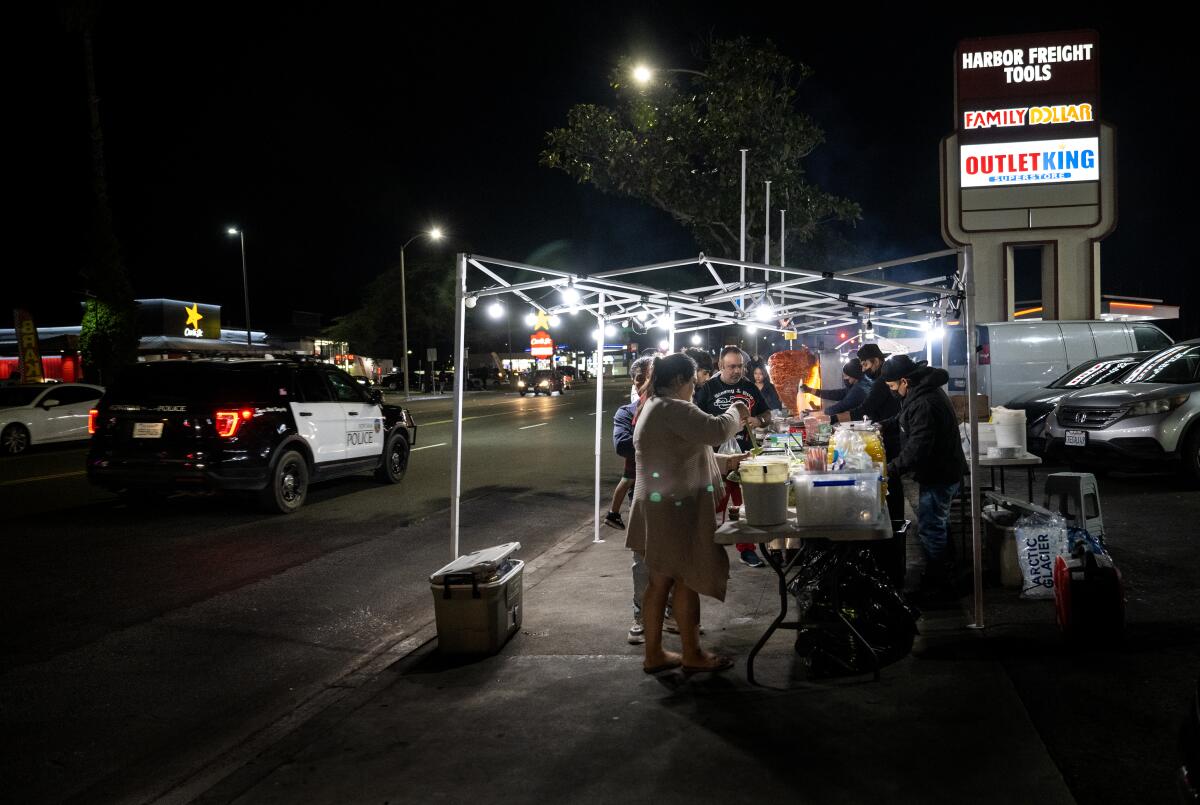 A police cruiser drives by a taco stand serving guests.