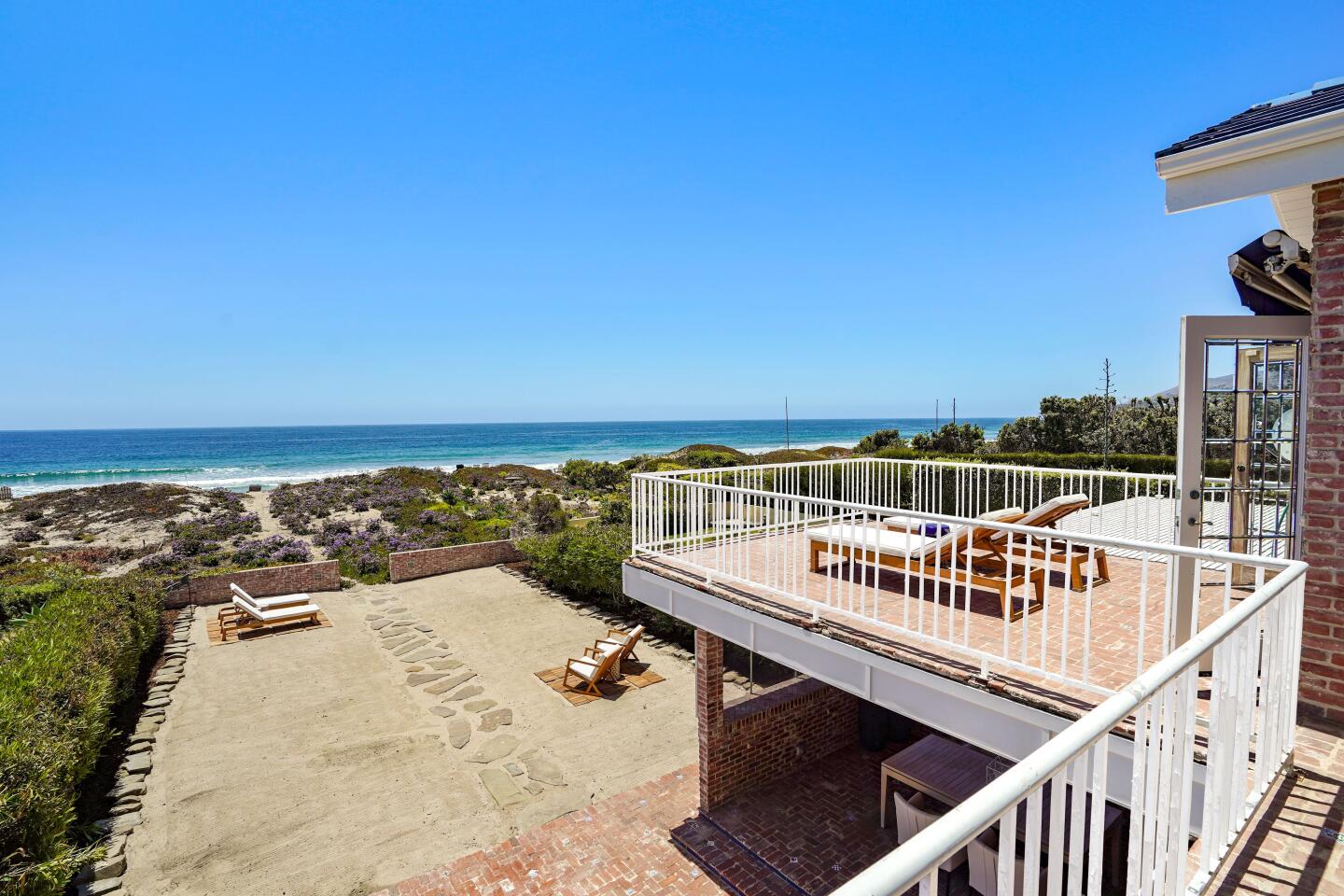 The deck with white railings overlooks the grounds and the ocean.