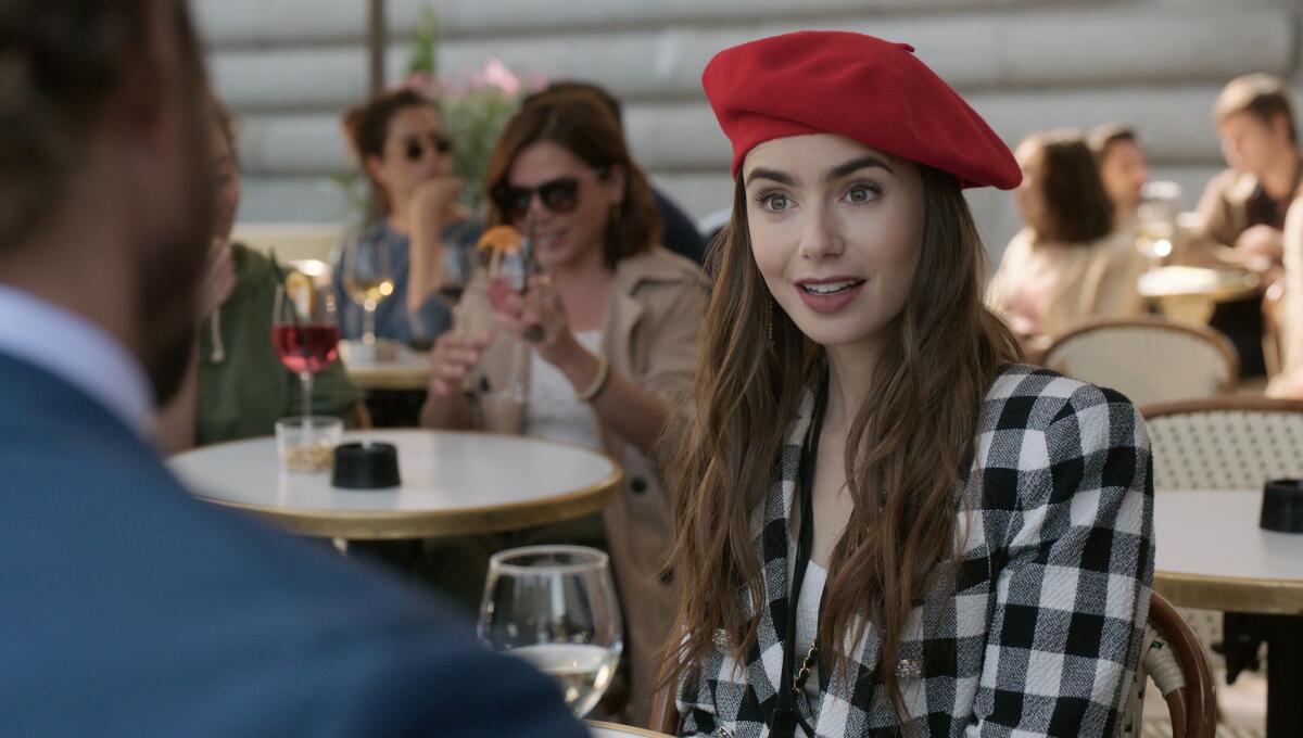 Lily Collins, in beret, sits at a cafe table with a glass of white wine in "Emily in Paris"