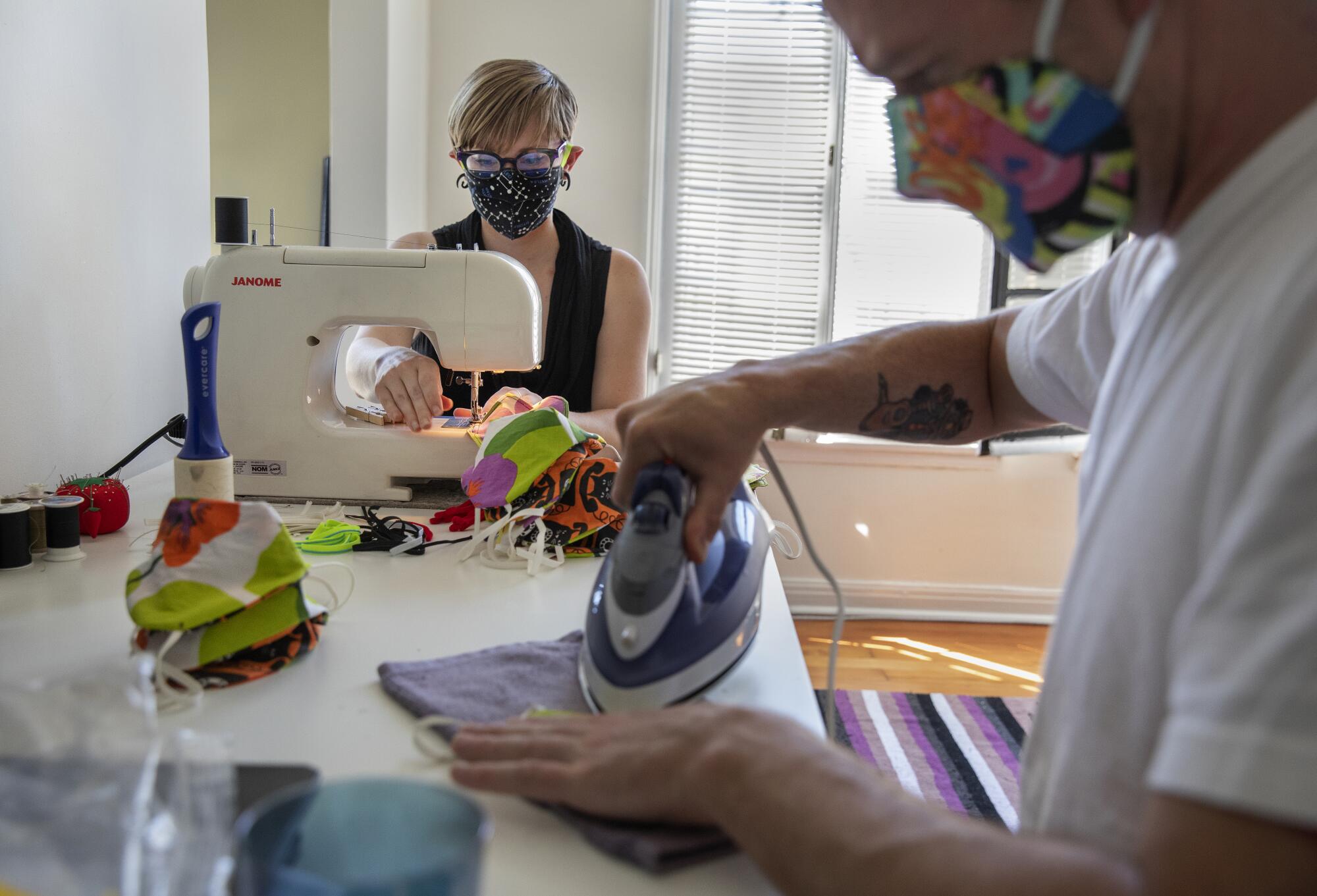 Rhea Aldridge, an out of work digital technician on photo shoots, sews masks at her home in East Hollywood. In foreground helping out with ironing the masks is her boyfriend, Jason Costello, a freelance graphic designer