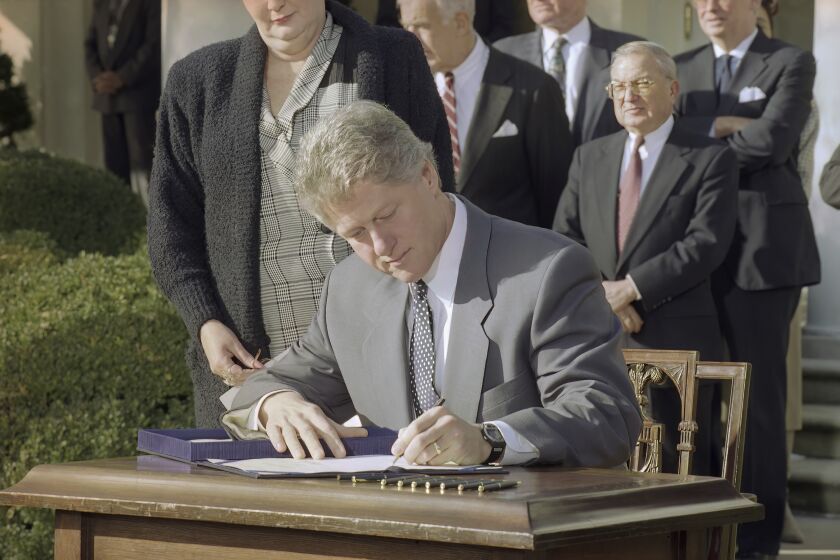 FILE - President Bill Clinton reaches for a pen as he signs the Family Leave Bill into law during a ceremony in the Rose Garden in Washington, Feb. 5, 1993. Looking over Clinton's shoulder is Vicki Yandle of Marietta, Ga., whose husband lost his job when he took off to take care of their sick daughter. Behind the President are House Speaker Tom Foley of Wash., Sen. Ted Kennedy, D-Mass., and Rep. William Ford, D-Mich. President Joe Biden is playing host to former President Bill Clinton to mark the 30th anniversary of the Family and Medical Leave Act. It was the first piece of legislation that Clinton signed into law after taking office in 1993. (AP Photo/Greg Gibson, File)
