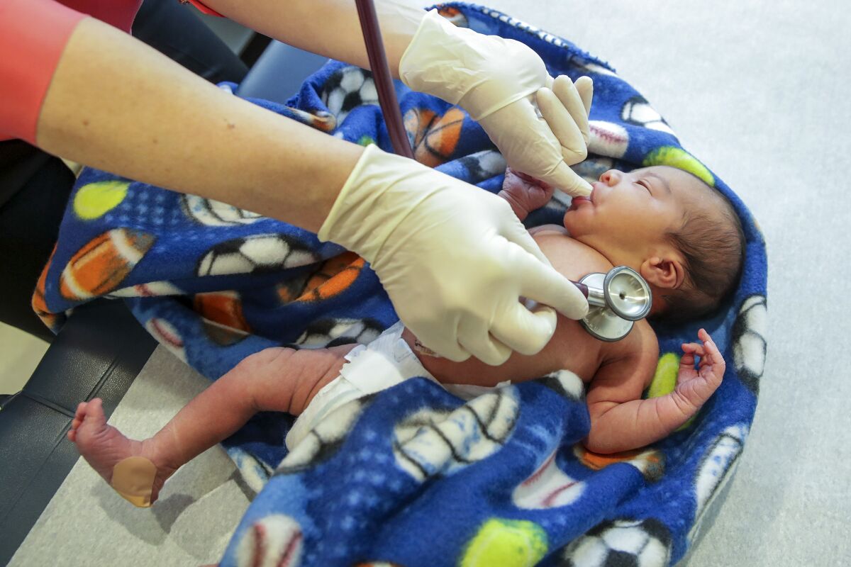 A doctor holds a stethoscope to a newborn baby's chest