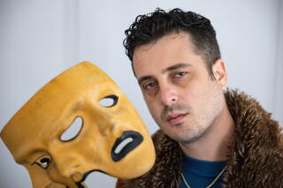 A man holds a three-faced mask.