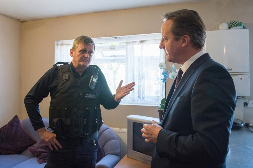 Prime Minister David Cameron, right, talks to Immigration Enforcement officer John Keane after police raided residential properties in London on May 21, looking for immigrants in the country illegally.
