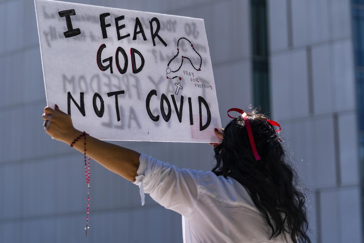 A woman holds a sign reading "I fear God not COVID."