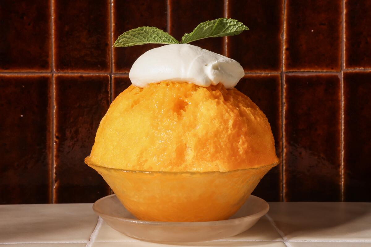 A large ball of mango Kakigori in a glass dish with whipped cream and mint on top