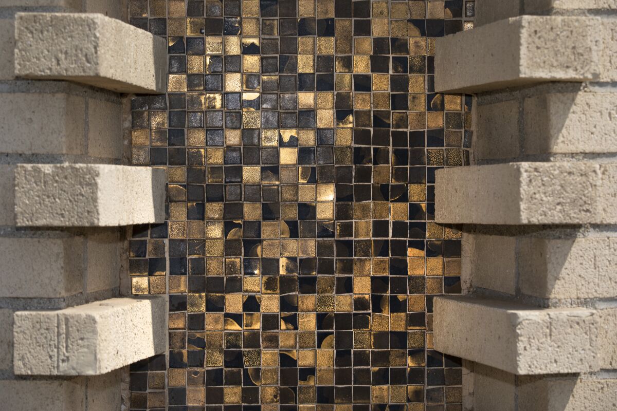 A close-up of the exterior of the YOLA Center shows sand-colored brick and black and gold mosaic details